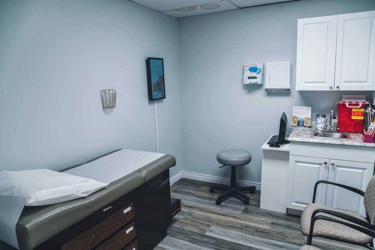A clean and organized medical exam room with an exam table, stool, and countertop supplies.